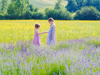Two girls sister sit between lavender fields in Provence. Violet lavender fields blooming in summer sunlight. Sea of Lilac Flowers landscape. Bunch of scented flowers of the French Provence