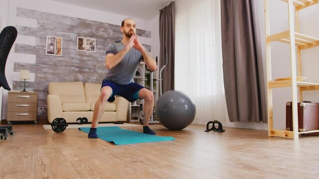 Athletic man training his legs doing squat exercise at home. Sport at home and healthy lifestyle, activity, fitness and workout. Indoor training and home exercise