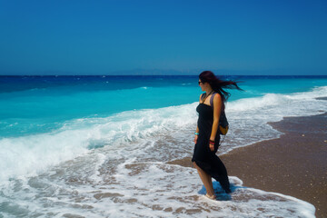 Sea wave washes legs of Happy woman traveler, the wind plays in her hair