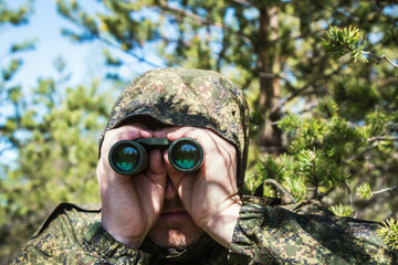 spy or scout looking through binoculars in the forest