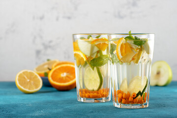 closeup orange water with sea buckthorn and mint in glasses on blue background, summmer drink concept