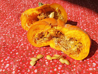 Broken pumpkin in half with scattered seeds on red material in the morning light.