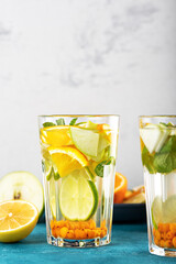 refreshing detox water with lemon, orange, mint in glasses on white blue background, summer lemonade concept, vertical