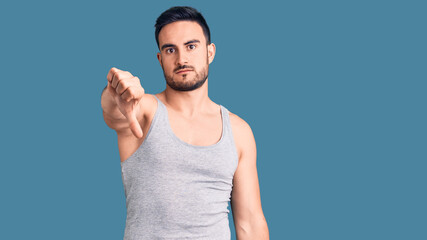 Young handsome man wearing swimwear and sleeveless t-shirt looking unhappy and angry showing...