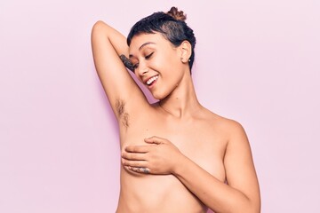 Young beautiful woman shirtless smiling happy. Standing with smile on face showing hairy armpit over isolated pink background - obrazy, fototapety, plakaty