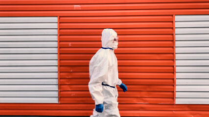 Man wearing protective COVID costume, mask, respirator and gloves. Doctor moving on red background. Pandemic, self-isolation and quarantine finish concept.