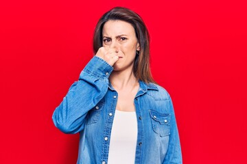 Young beautiful woman wearing casual clothes smelling something stinky and disgusting, intolerable smell, holding breath with fingers on nose. bad smell