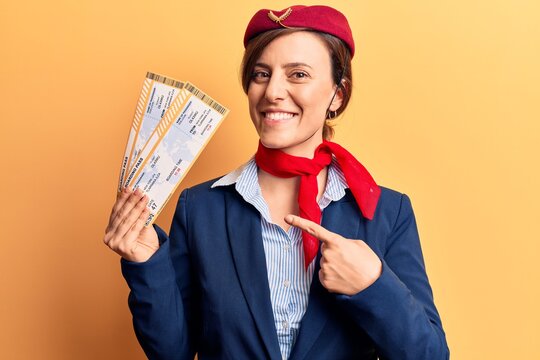 Young beautiful woman wearing stewardess uniform holding boarding pass smiling happy pointing with hand and finger