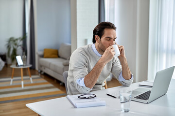 Young businessman enjoying in cup of coffee while talking on the phone at home.