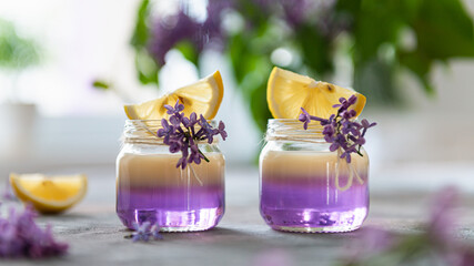 Alcoholic shot cocktails with vanilla liqour in tiny jars on gray concrete background. Summer party. Shot drinks with lilac on the background. Bar menu