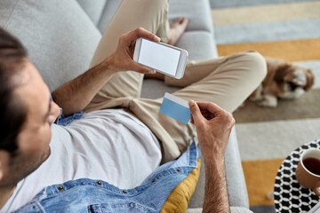 Close-up of a man using credit card and cell phone while e-banking from home.