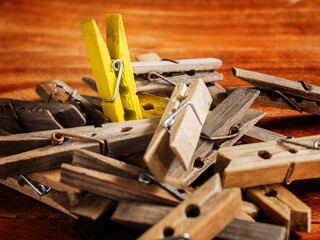 One yellow painted wooden washing line clothes peg stands out in a pile of plain clothes pegs