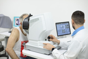 Doctor Optometrist examining bearded senior man eyes with special eye equipment.