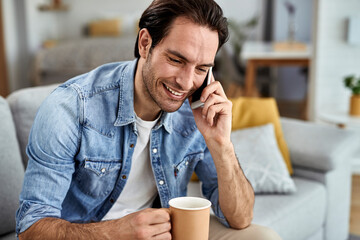 Happy man making a phone call while drinking coffee in the living room.