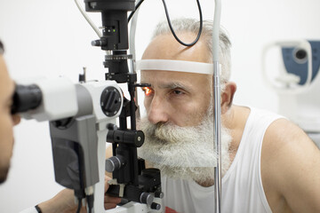 Doctor Optometrist examining bearded senior man eyes with special eye equipment.