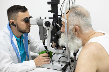 Doctor Optometrist examining bearded senior man eyes with special eye equipment.