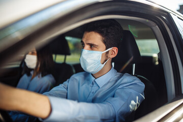 Fototapeta na wymiar Young man taxi driver wears sterile medical mask in the car. A boy behind the car steering wheel safely driving for business matter keeping social distance. Coronavirus pandemic concept.
