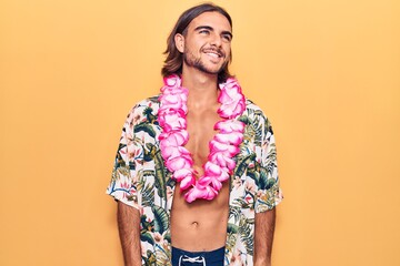 Young handsome man wearing swimwear and hawaiian lei looking away to side with smile on face, natural expression. laughing confident.