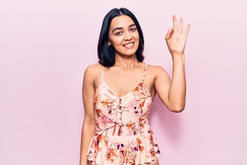 Young beautiful latin woman wearing casual clothes smiling positive doing ok sign with hand and...