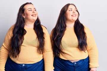 Young plus size twins wearing casual clothes looking away to side with smile on face, natural...