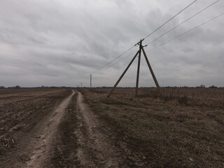 Fototapeta na wymiar Power lines along a dirt road. Gloomy evening landscape.