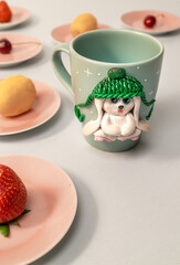 The original mug with decorative figurines made with their own hands. Figures on the cup are fashioned hand made from colored clay. Fruits and berries on a plates around. High quality photo