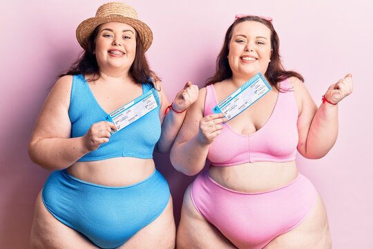 Young plus size twins wearing bikini holding boarding pass screaming proud, celebrating victory and success very excited with raised arm