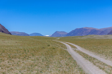 Fototapeta na wymiar Winding dirt road through lush rolling hills of Central Mongolian steppe. Mongolian Altai