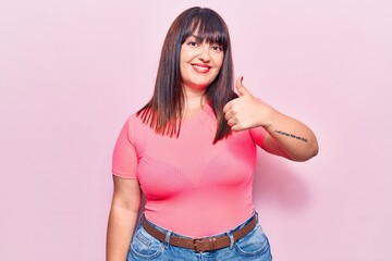 Young plus size woman wearing casual clothes doing happy thumbs up gesture with hand. approving expression looking at the camera showing success.
