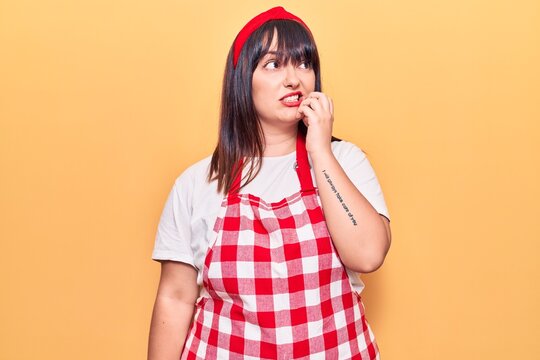 Young plus size woman wearing apron looking stressed and nervous with hands on mouth biting nails. anxiety problem.