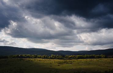 Dramatic sky with dark rain clouds and sunshine illuminating green slopes