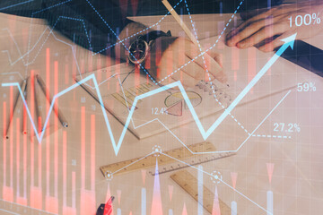 Double exposure of man's hands writing notes of stock market with forex chart.