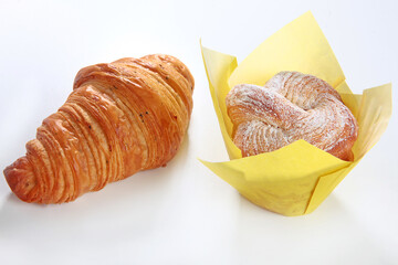 Croissant and cupcake in parchment paper on a white background. An isolated object. Copy of the space. An isolated object.