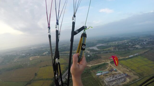 Person on motorized parachute as adrenaline and extreme sport activity falling from sky with open fileds and mountaind at the background. Pilot man on the paraglider point of view shot.