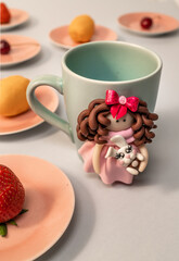 The original mug with decorative figurines made with their own hands. Figures on the cup are fashioned hand made from colored clay. Fruits and berries on a plates around. High quality photo