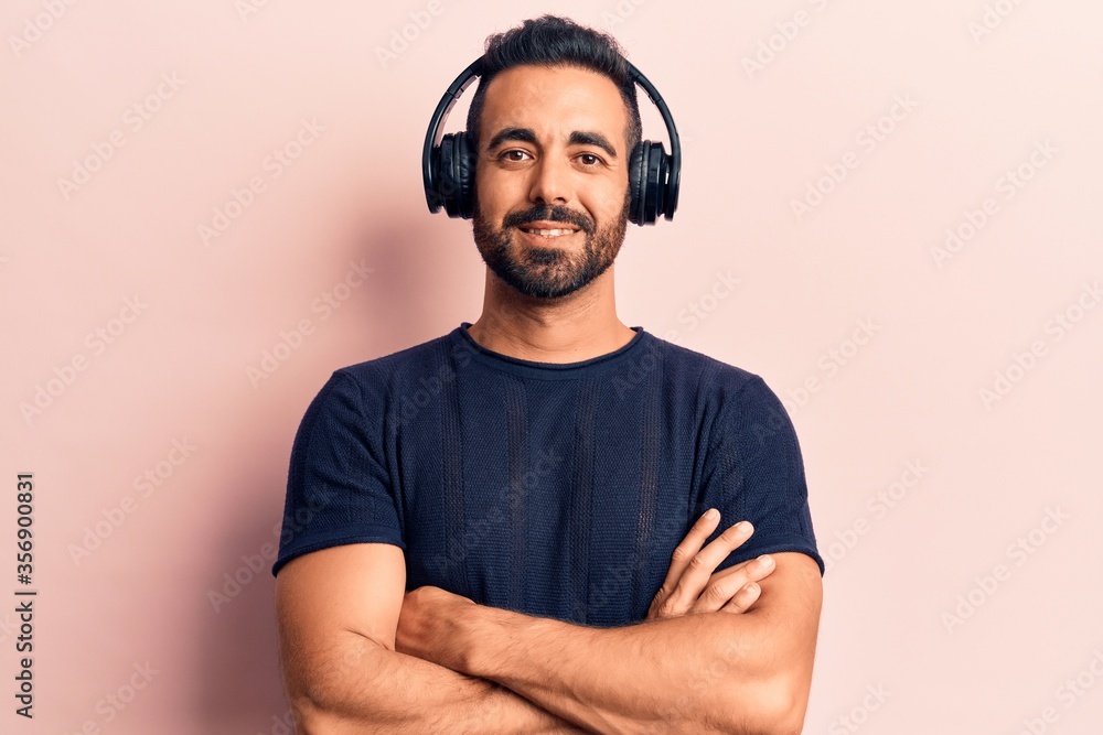 Sticker young hispanic man listening to music using headphones happy face smiling with crossed arms looking 