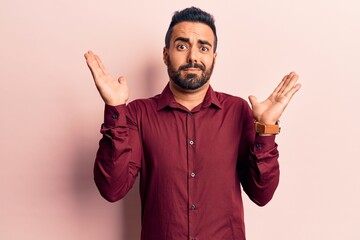 Young hispanic man wearing casual clothes clueless and confused with open arms, no idea and...