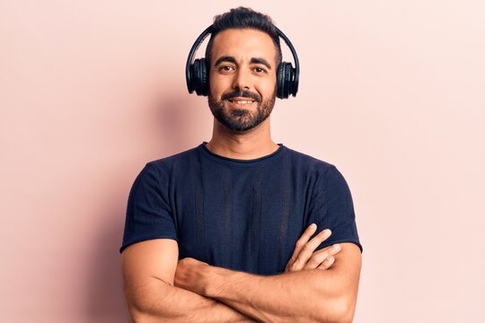 Young hispanic man listening to music using headphones happy face smiling with crossed arms looking at the camera. positive person.