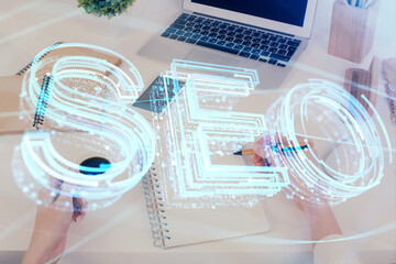 Multi exposure of woman's hands making notes with SEO icon. Concept of Search engine optimization