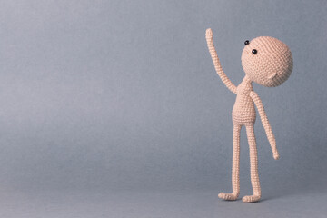 A toy man on a gray background with space for text. Knitted toy amigurumi. Cute model. Puppet. Sweet doll. Blank for a booklet, poster, presentation, banner. Hand up. Looks up. He points up.