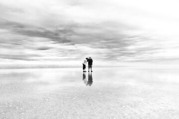 two old people walking along the Eighty Miles Beach in Western Australia, in a claudy day where the beach seemed a mirror