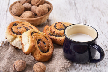 Basket of homemade buns with jam, served on old wooden table with walnuts and cup of milk
