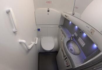 Bathroom of a passenger aircraft Boeing 737. Toilet bowl, sink, knob to drain water, seatcovers, handrails