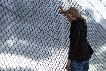 Sad depressed young business woman alone leaning against barbed wire fence on a cloudy day....
