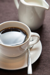 Black coffee in a cup and saucer, next to a white jug of milk.