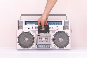 Hand inserting a tape of music into the deck of a vintage 80s radio cassette. Play music concept.
