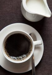 Black coffee in a cup and saucer, next to a white jug of milk.