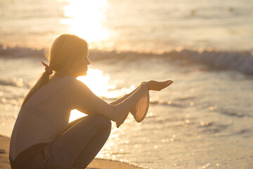 Calm and peaceful young woman sitting alone on the beach sand during a beautiful sunset reflecting...