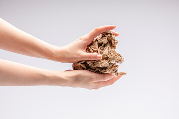 Close-up of a white people's hand holding a crumpled piece of brown paper in front of a white background