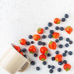 Fototapeta na wymiar Fresh organic blueberry and strawberry in enameled mug on vintage white stone table.